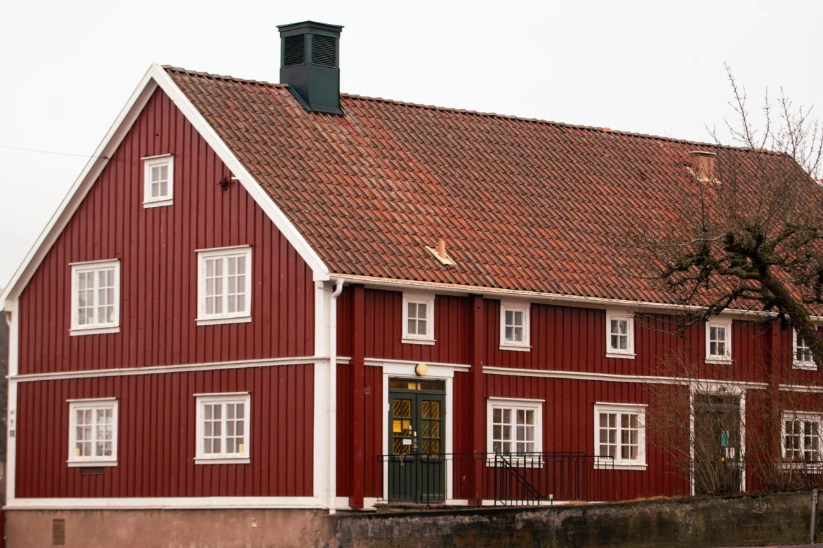 Rödmålat trähus med vita fönsterfoder och tegeltak i klassisk svensk stil.
